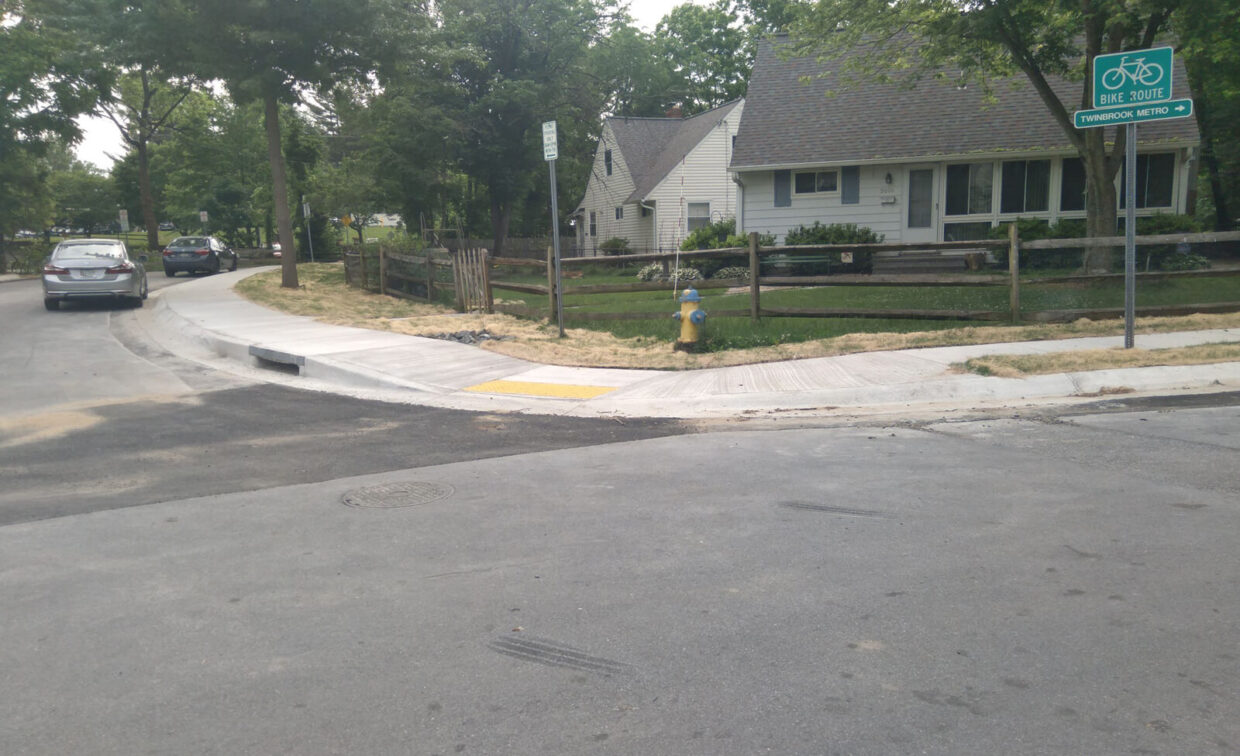 A newly paved sidewalk with a curb ramp and yellow tactile paving leads to a house; a fire hydrant and a